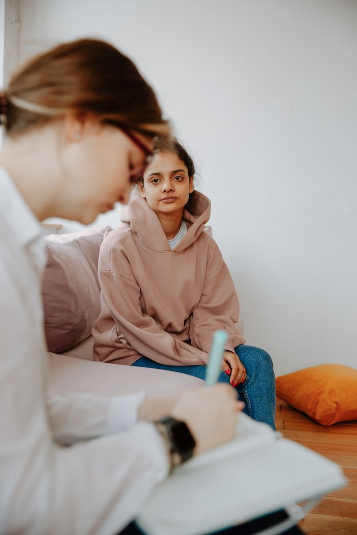 Therapist taking notes while young woman shares her thoughts in a counseling session.