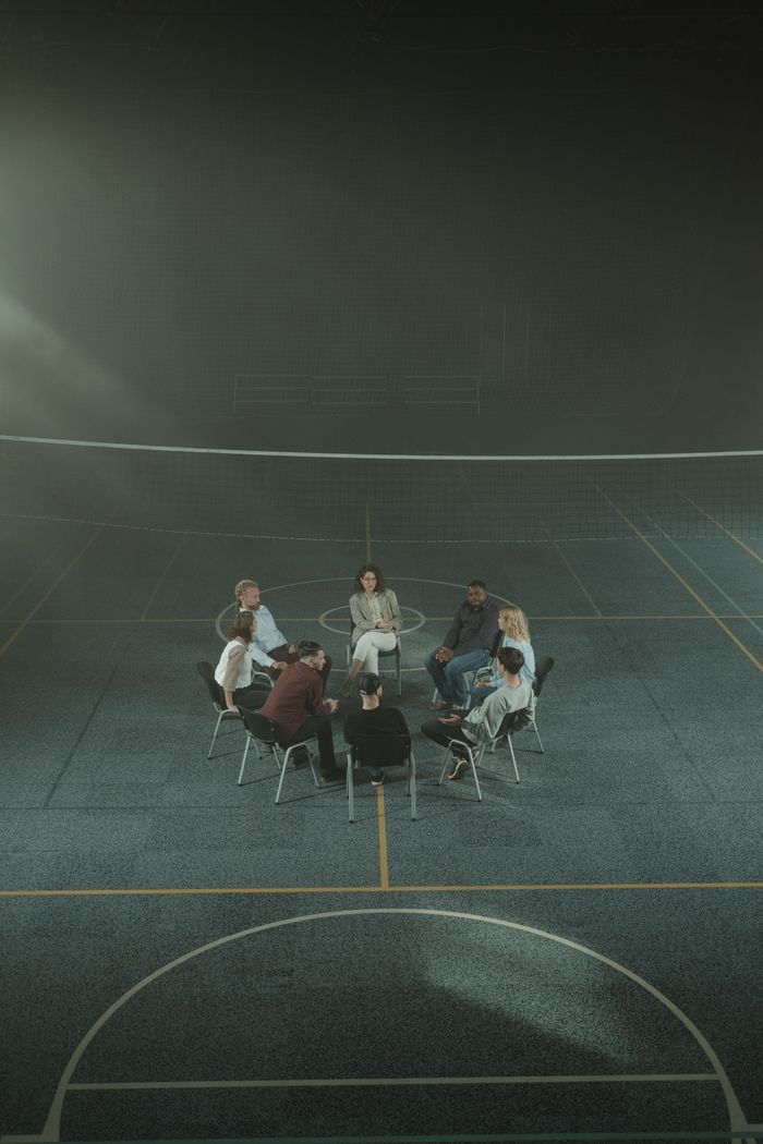 Multicultural support group sitting in a circle in a gym, discussing personal issues.
