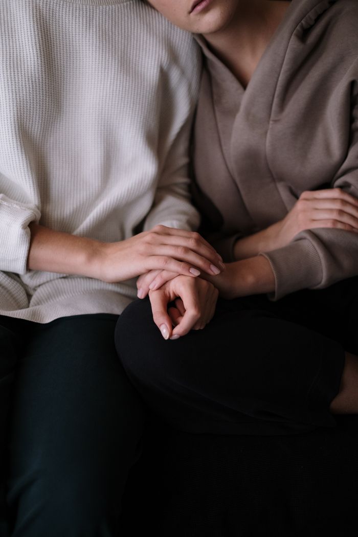 Intimate close-up of two adults sitting together, gently holding hands in a comforting gesture.